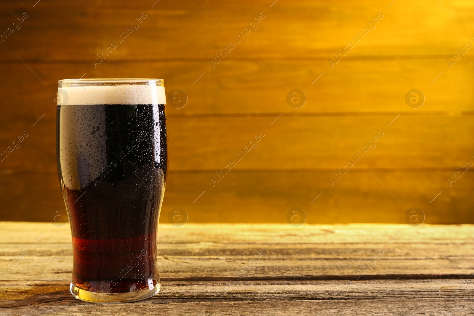 Photo of Glass of beer with froth on wooden table, space for text