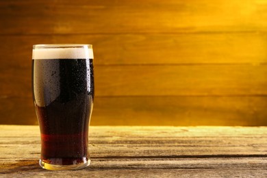 Glass of beer with froth on wooden table, space for text