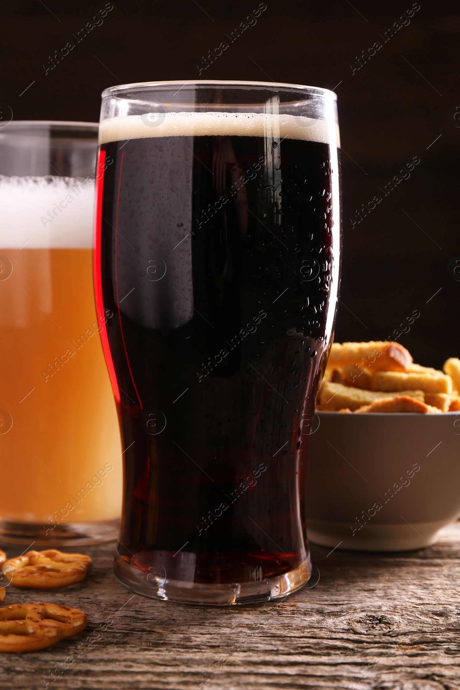 Photo of Glasses of beer, pretzel crackers and rusks on wooden table, closeup