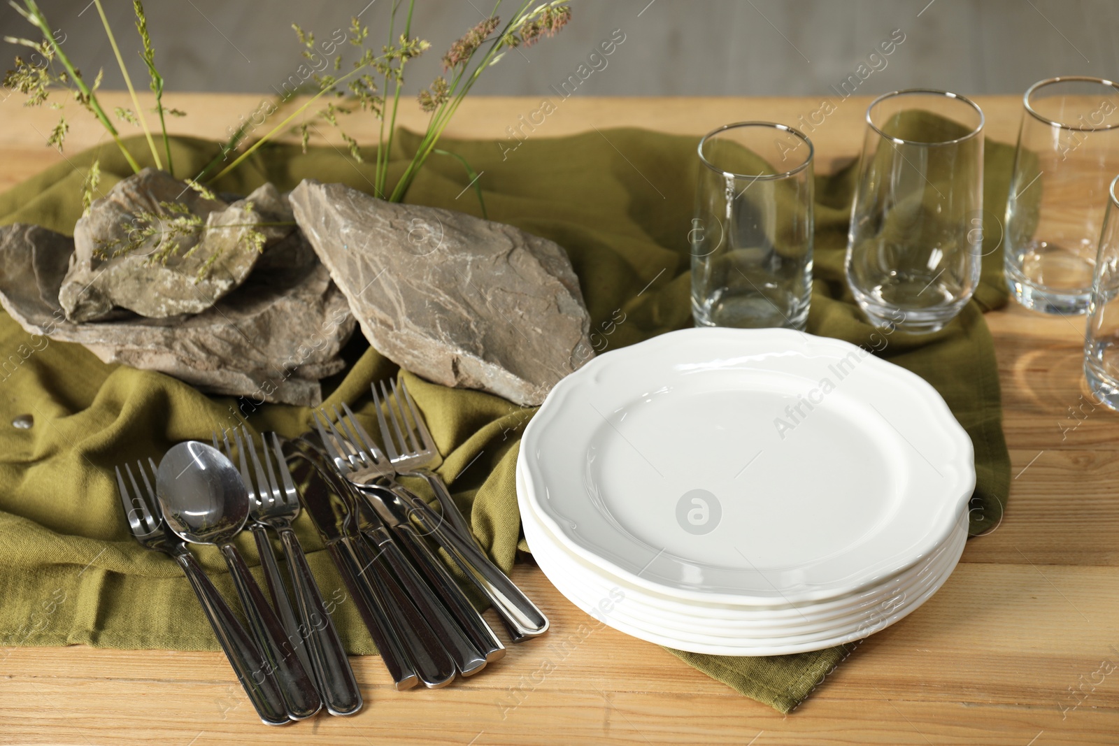 Photo of Clean dishes, stones and plants on wooden table in dining room, closeup