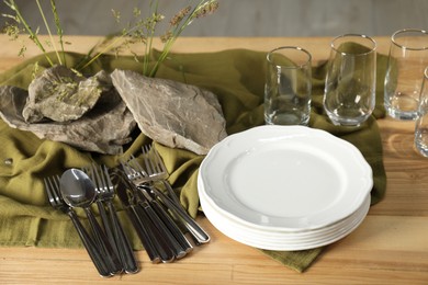 Clean dishes, stones and plants on wooden table in dining room, closeup