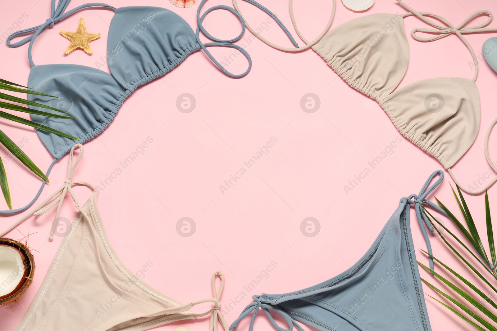 Photo of Frame of beautiful swimsuits and palm leaves on pink background, flat lay. Space for text