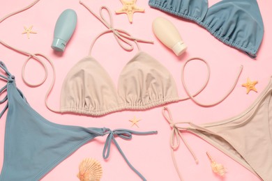 Photo of Beautiful swimsuits, seashells and sunscreens on pink background, flat lay