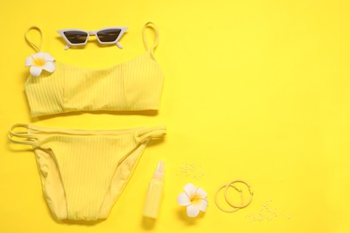 Beautiful swimsuit, sunglasses and sunscreen on yellow background, flat lay. Space for text