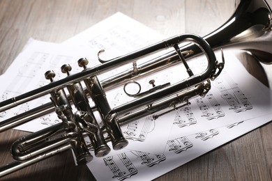 Photo of Trumpet and music sheet papers with notes on wooden table, closeup