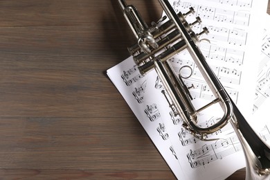 Trumpet and music sheet papers with notes on wooden table, top view. Space for text