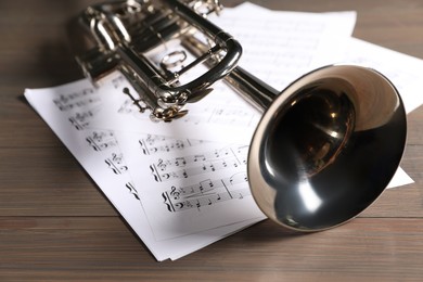 Trumpet and music sheet papers with notes on wooden table, closeup