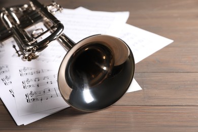 Trumpet and music sheet papers with notes on wooden table, closeup