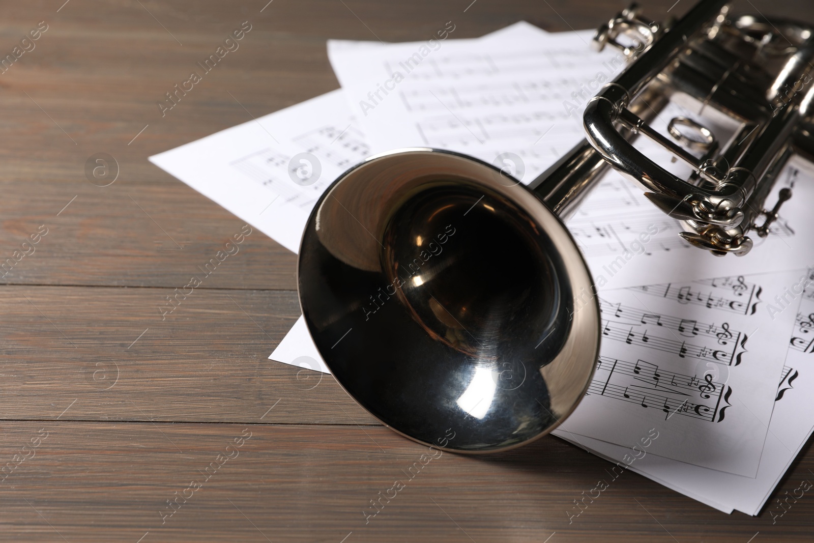 Photo of Trumpet and music sheet papers with notes on wooden table, closeup. Space for text