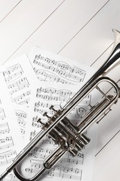 Trumpet and music sheet papers with notes on white wooden table, flat lay