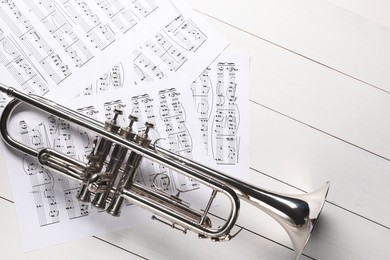 Trumpet and music sheet papers with notes on white wooden table, flat lay