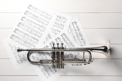 Trumpet and music sheet papers with notes on white wooden table, flat lay