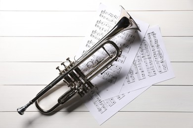 Trumpet and music sheet papers with notes on white wooden table, flat lay