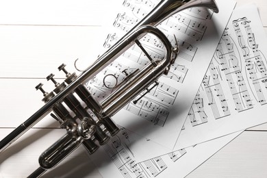 Photo of Trumpet and music sheet papers with notes on white wooden table, flat lay