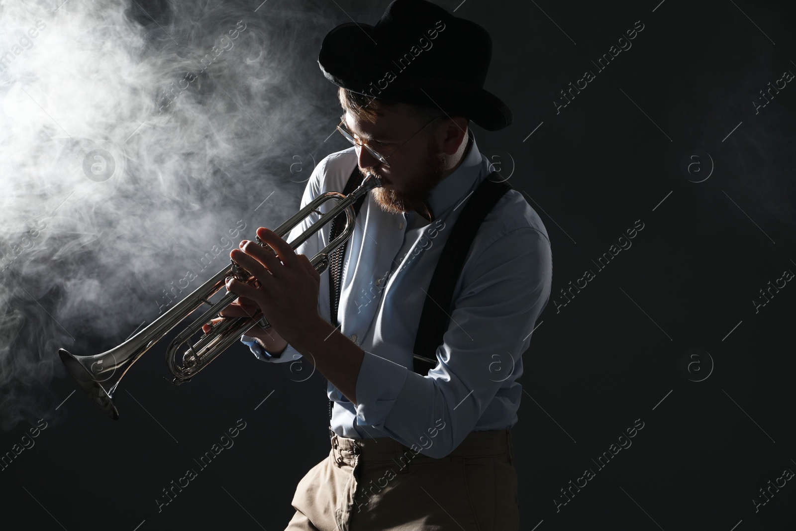 Photo of Professional musician playing trumpet on black background with smoke