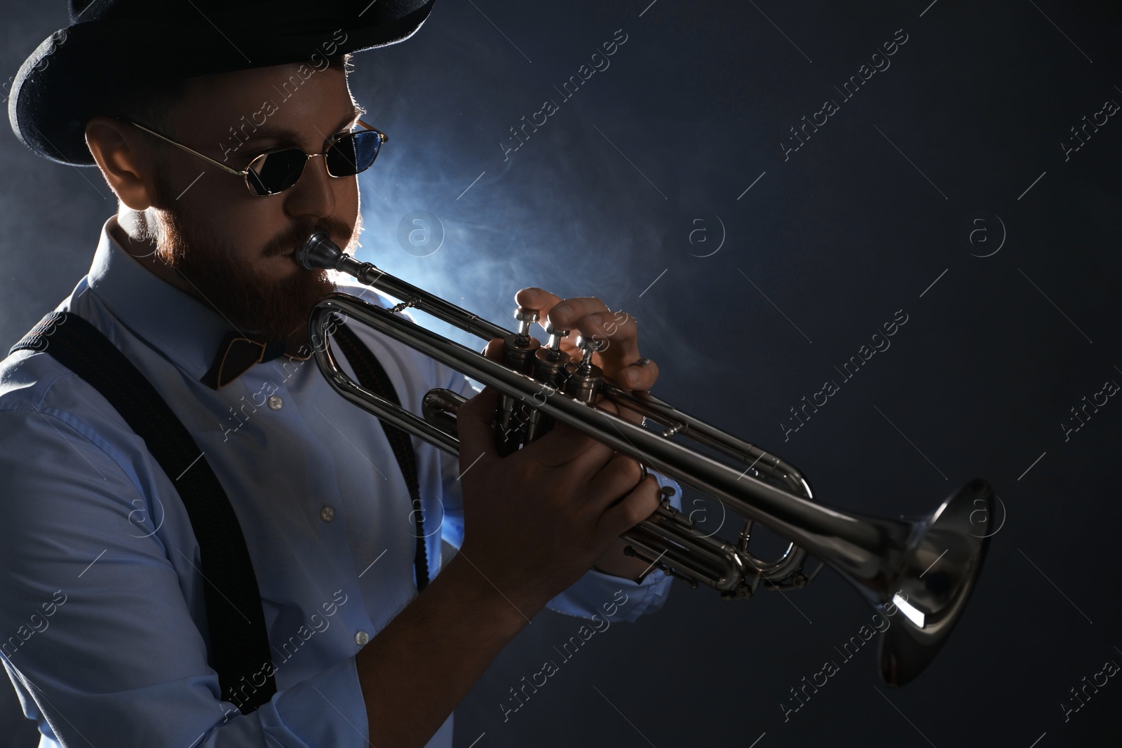 Photo of Professional musician playing trumpet on dark background with smoke