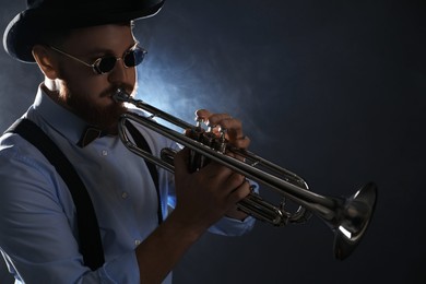 Professional musician playing trumpet on dark background with smoke