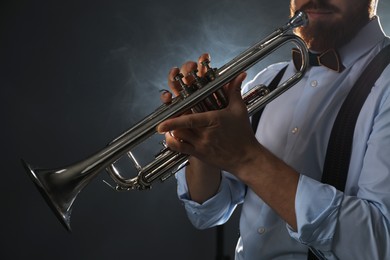 Professional musician holding trumpet on dark background, closeup