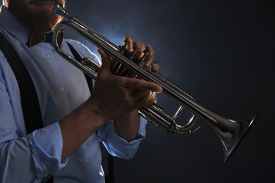 Professional musician holding trumpet on dark background, closeup