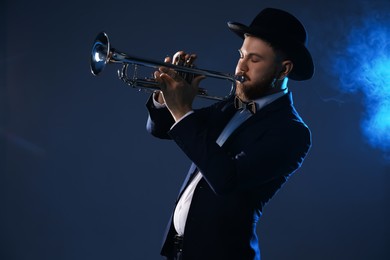 Photo of Professional musician playing trumpet on dark background in blue lights and smoke