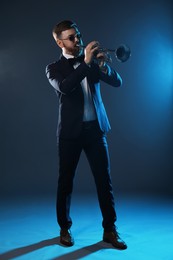 Photo of Professional musician playing trumpet on dark background in blue lights
