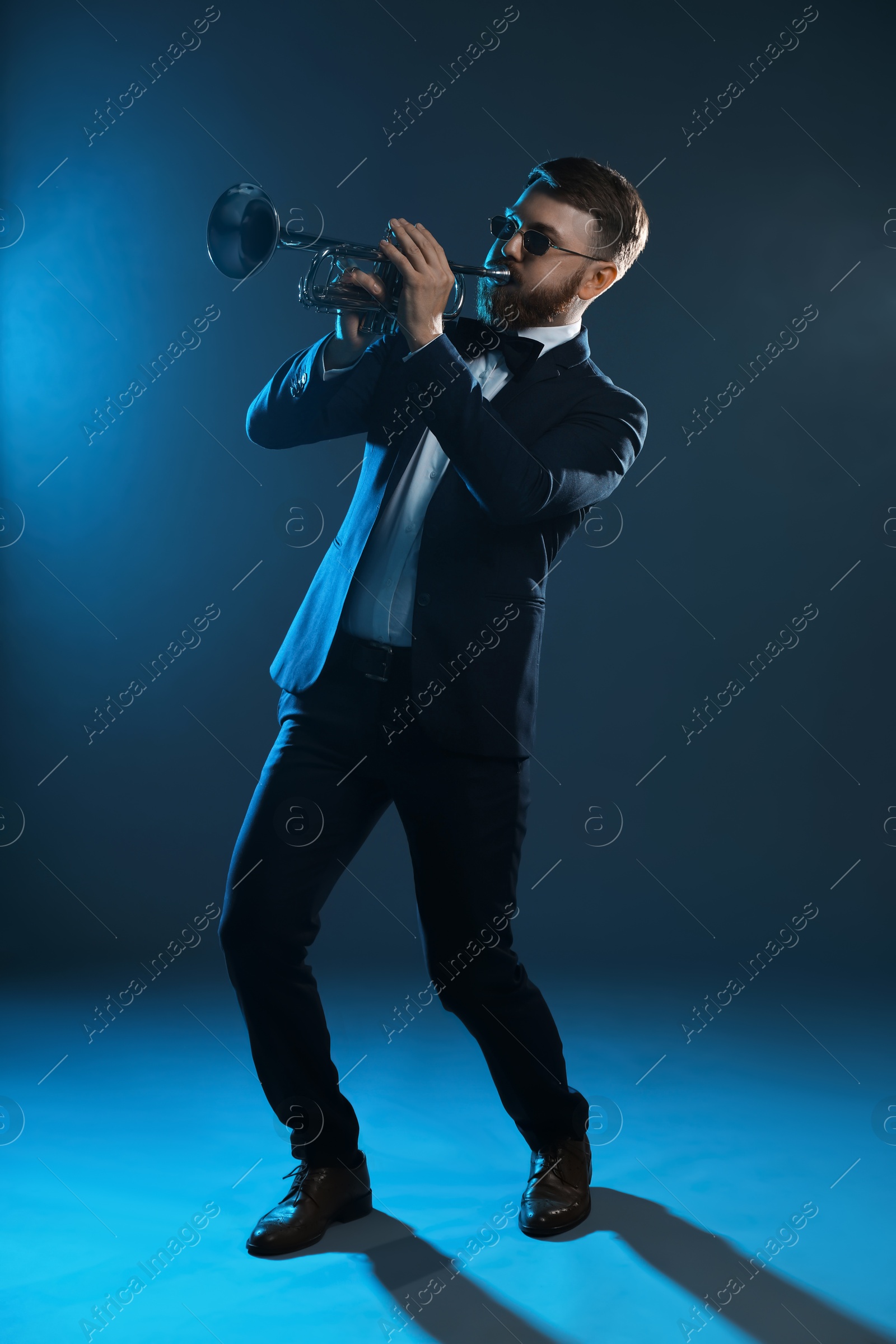 Photo of Professional musician playing trumpet on dark background in blue lights