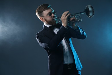 Photo of Professional musician playing trumpet on dark background in smoke