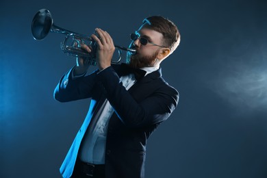 Professional musician playing trumpet on dark background in smoke