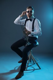 Photo of Handsome musician with trumpet sitting on stool against dark background