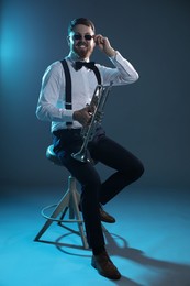 Photo of Smiling musician with trumpet sitting on stool against dark background