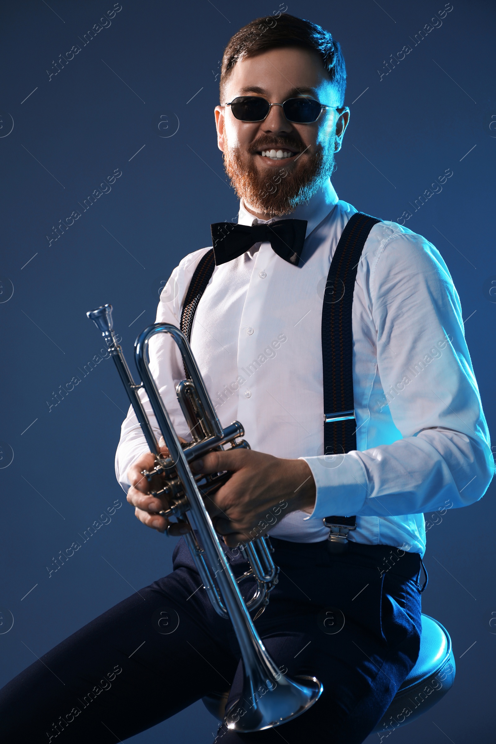 Photo of Smiling musician with trumpet sitting against dark background