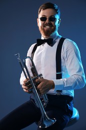 Photo of Smiling musician with trumpet sitting against dark background