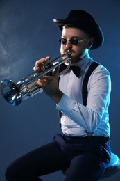 Photo of Professional musician playing trumpet on dark background with smoke