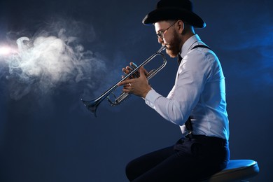 Photo of Professional musician playing trumpet on dark background with smoke, space for text