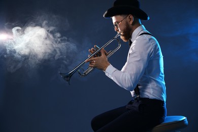 Professional musician playing trumpet on dark background with smoke, space for text