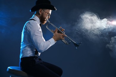 Photo of Professional musician playing trumpet on dark background with smoke, space for text