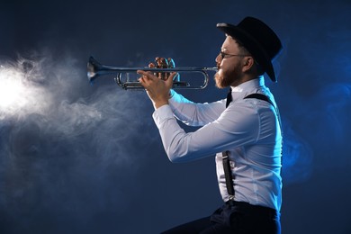 Photo of Professional musician playing trumpet on dark background with smoke, space for text