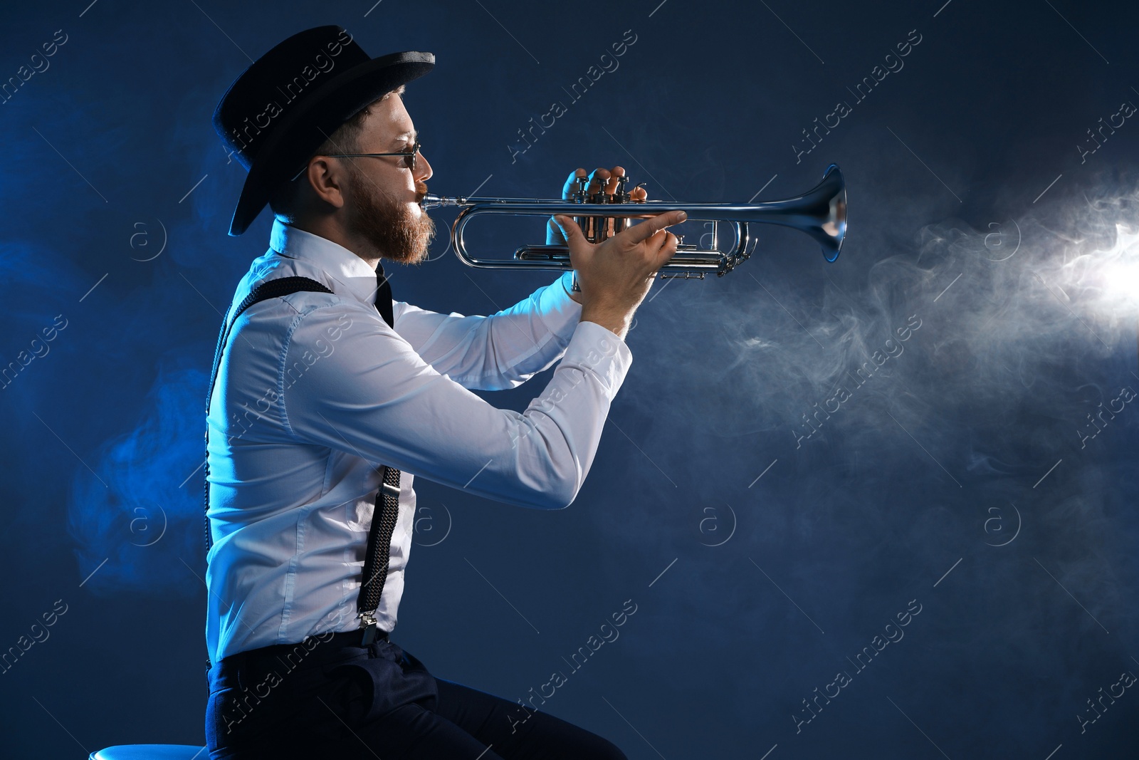 Photo of Professional musician playing trumpet on dark background with smoke, space for text