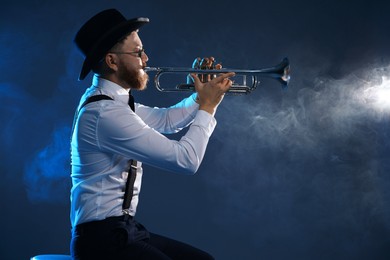 Photo of Professional musician playing trumpet on dark background with smoke, space for text