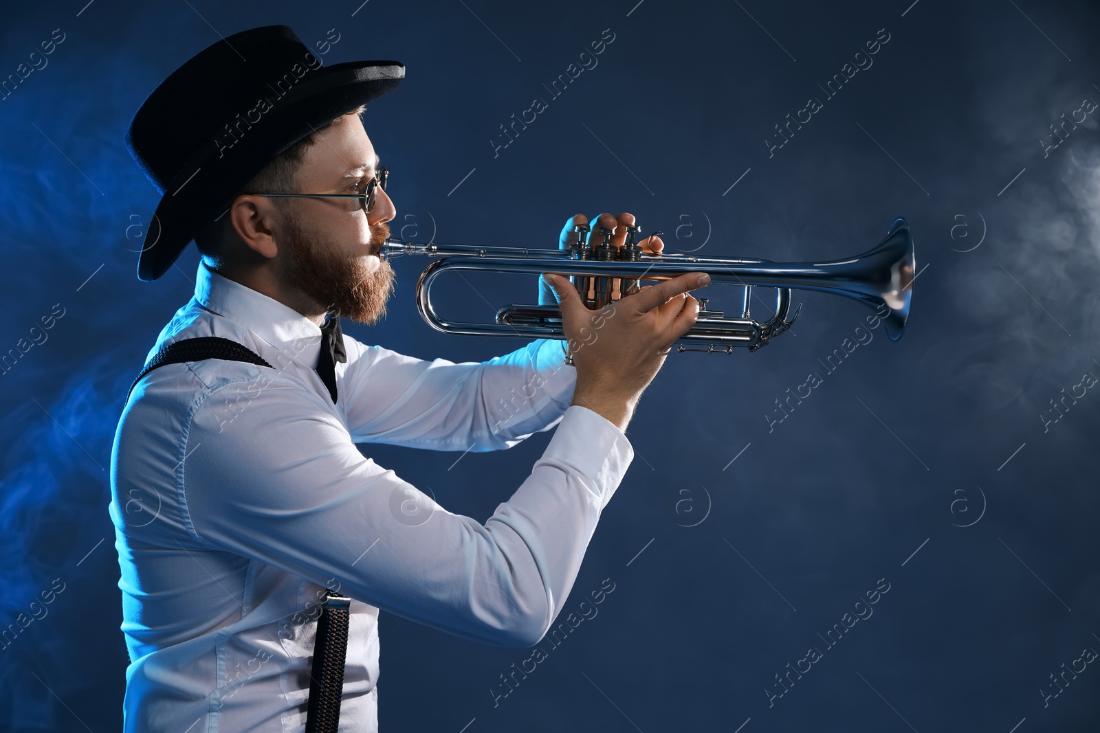 Photo of Professional musician playing trumpet on dark background with smoke