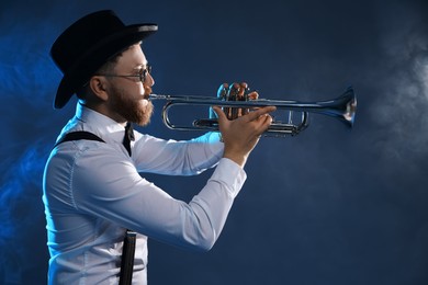 Professional musician playing trumpet on dark background with smoke