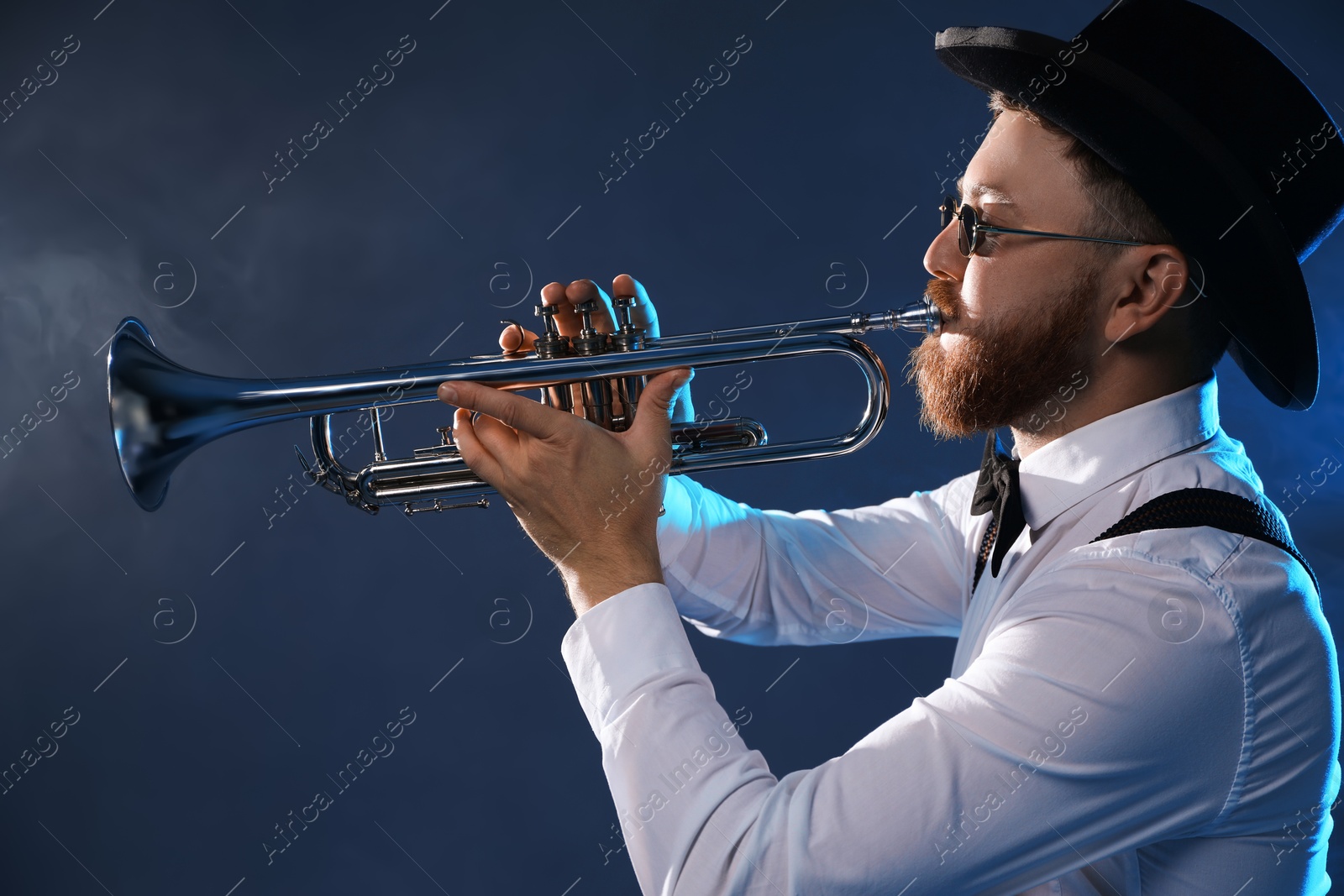 Photo of Professional musician playing trumpet on dark background with smoke