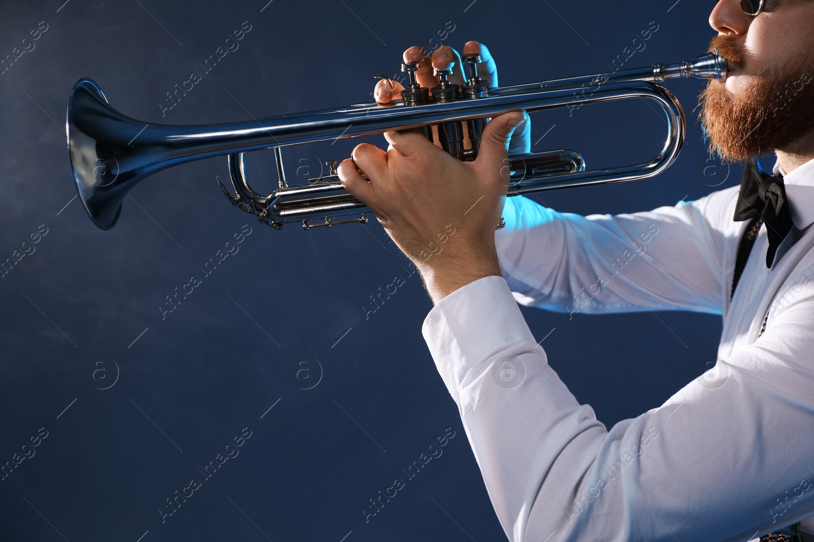 Photo of Professional musician playing trumpet on dark background with smoke, closeup