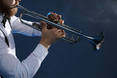 Photo of Professional musician playing trumpet on dark background with smoke, closeup