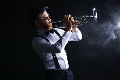 Professional musician playing trumpet on black background with smoke