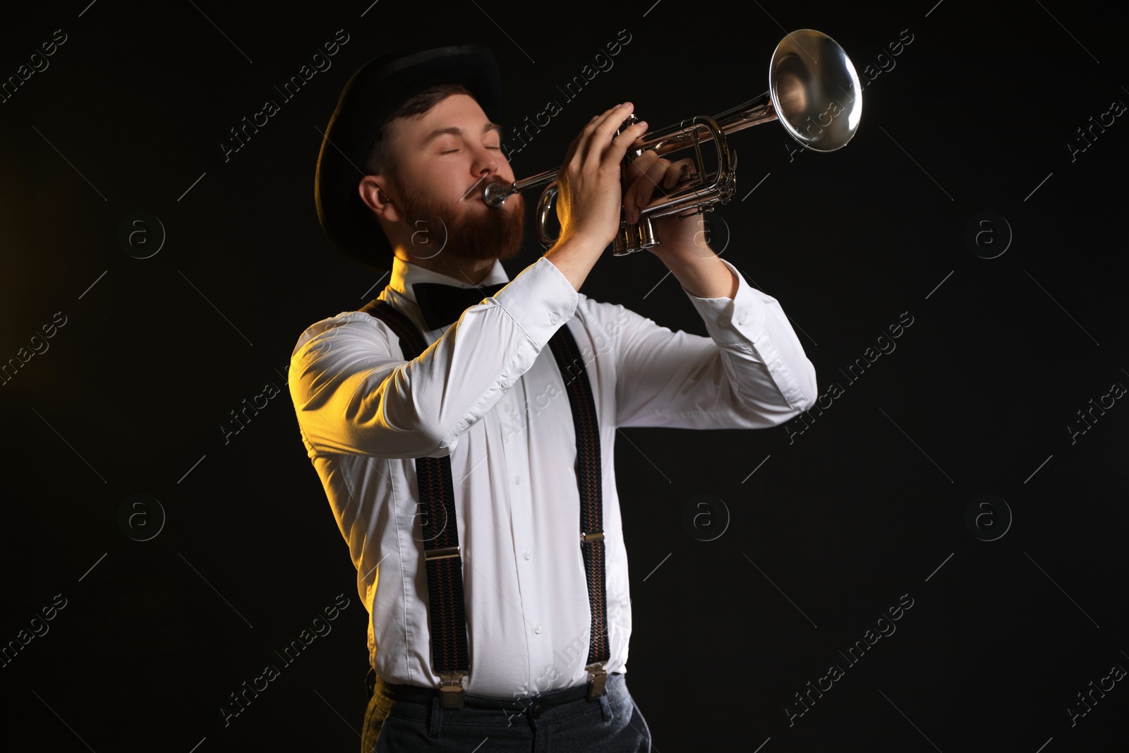 Photo of Professional musician playing trumpet on black background in color lights