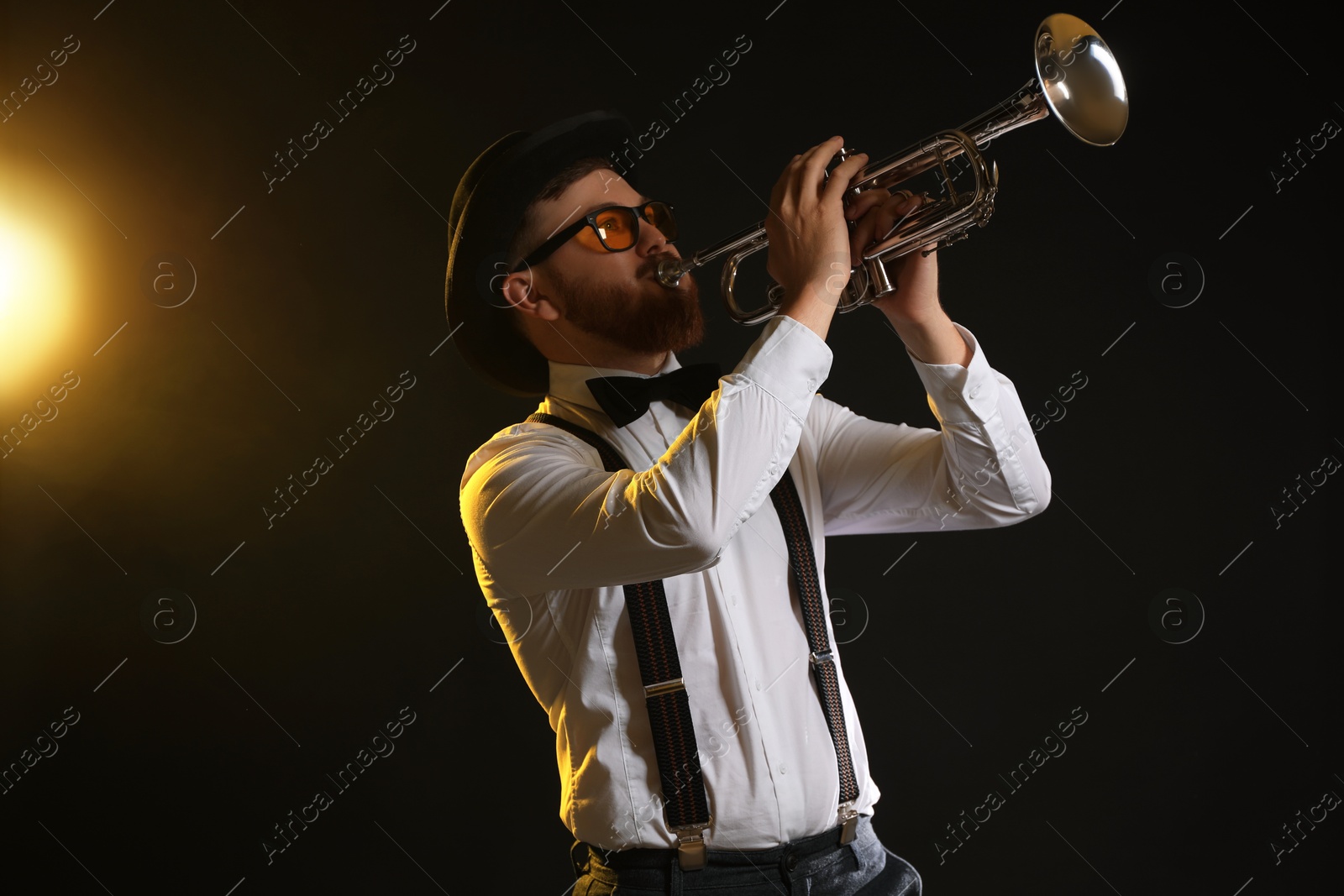 Photo of Professional musician playing trumpet on black background in color lights