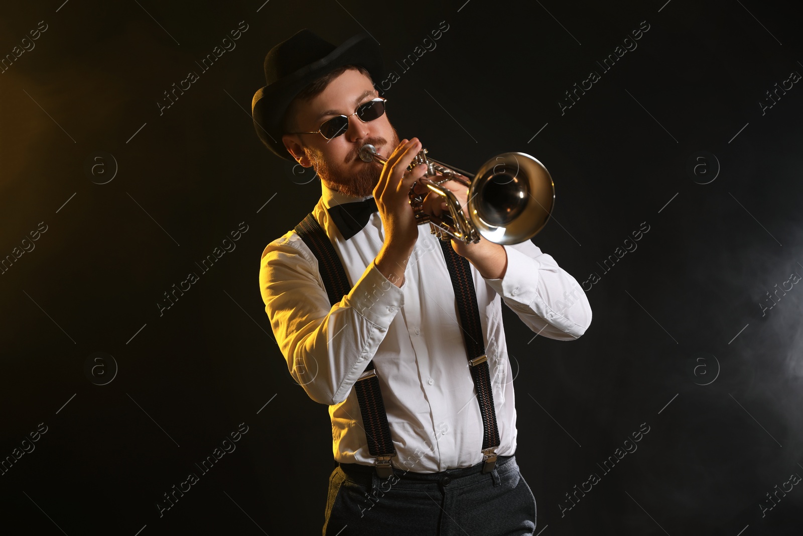 Photo of Professional musician playing trumpet on black background in color lights