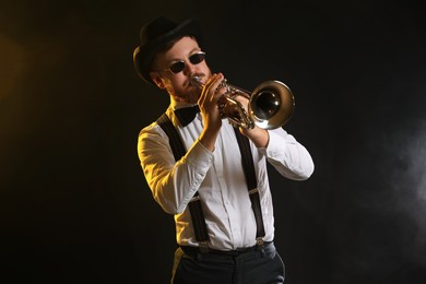 Professional musician playing trumpet on black background in color lights