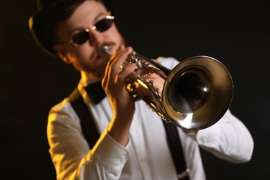 Photo of Professional musician playing trumpet on black background in color lights, selective focus